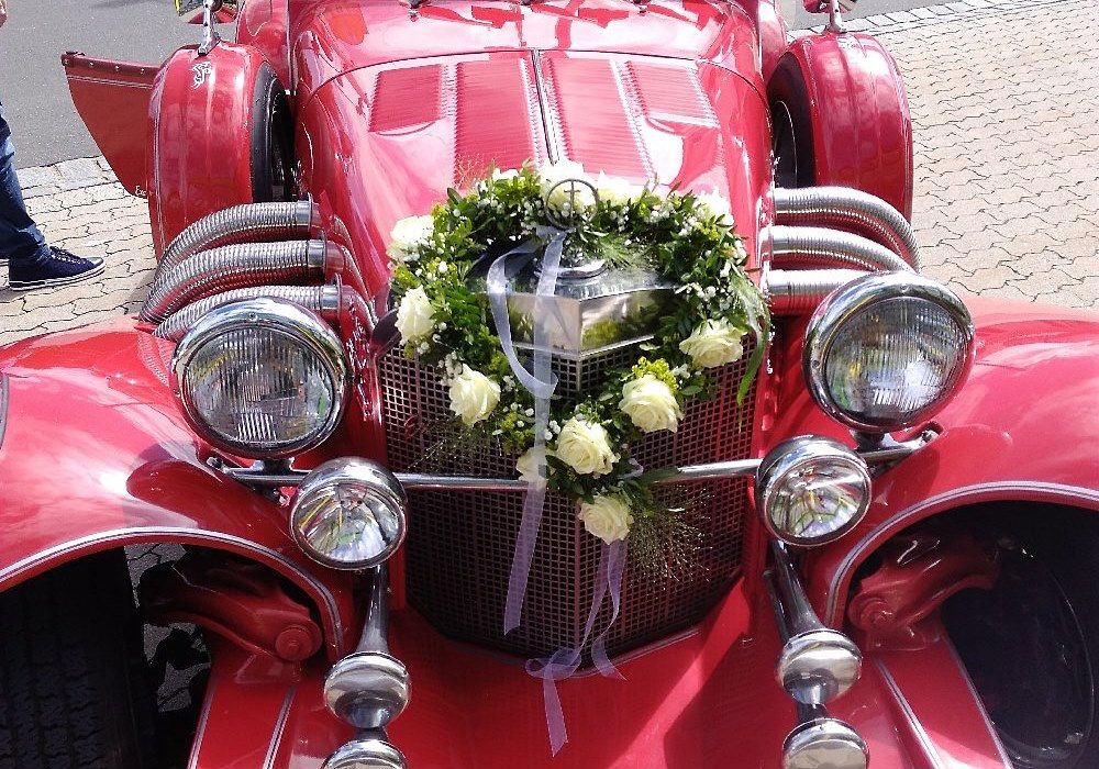 Herzförmige Blumenkomposition mit cremefarbenen Blüten auf einem roten Oldtimer platziert