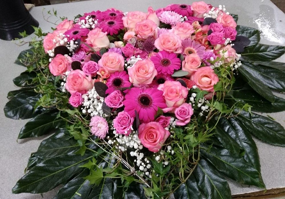 Herzförmige Blumenkomposition mit rosanen und pinken Blüten auf einem schwarzen Untergrund